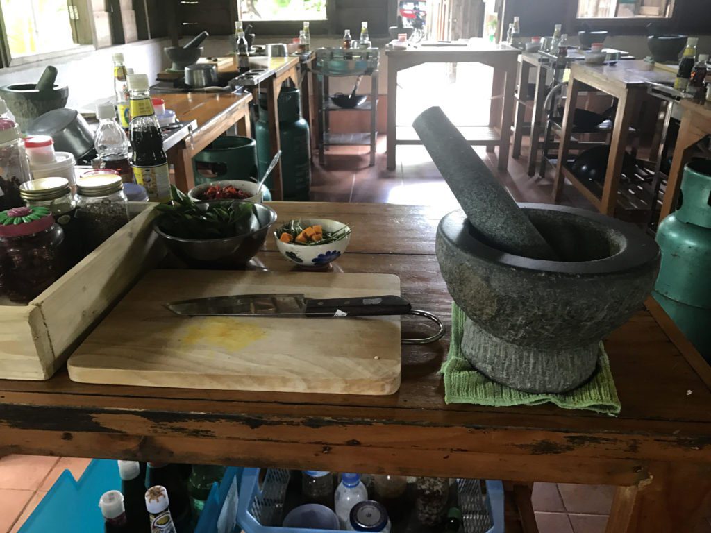 A table with a mortar and pestle, cutting board and knife, and other cooking utensils and ingredients