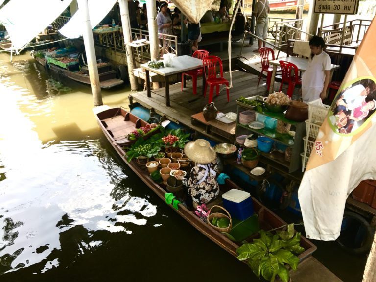 Woman preparing food while sitting in a boat in a floating market in Thailand