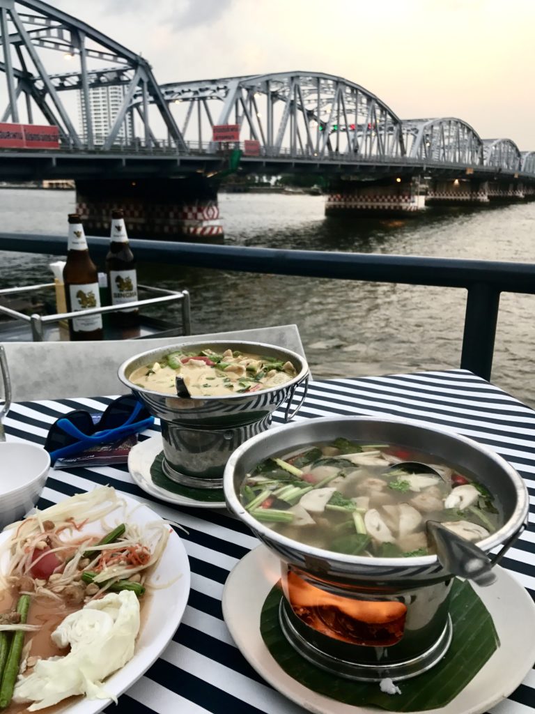 Thai beers and food on a table outside overlooking a bridge and a river