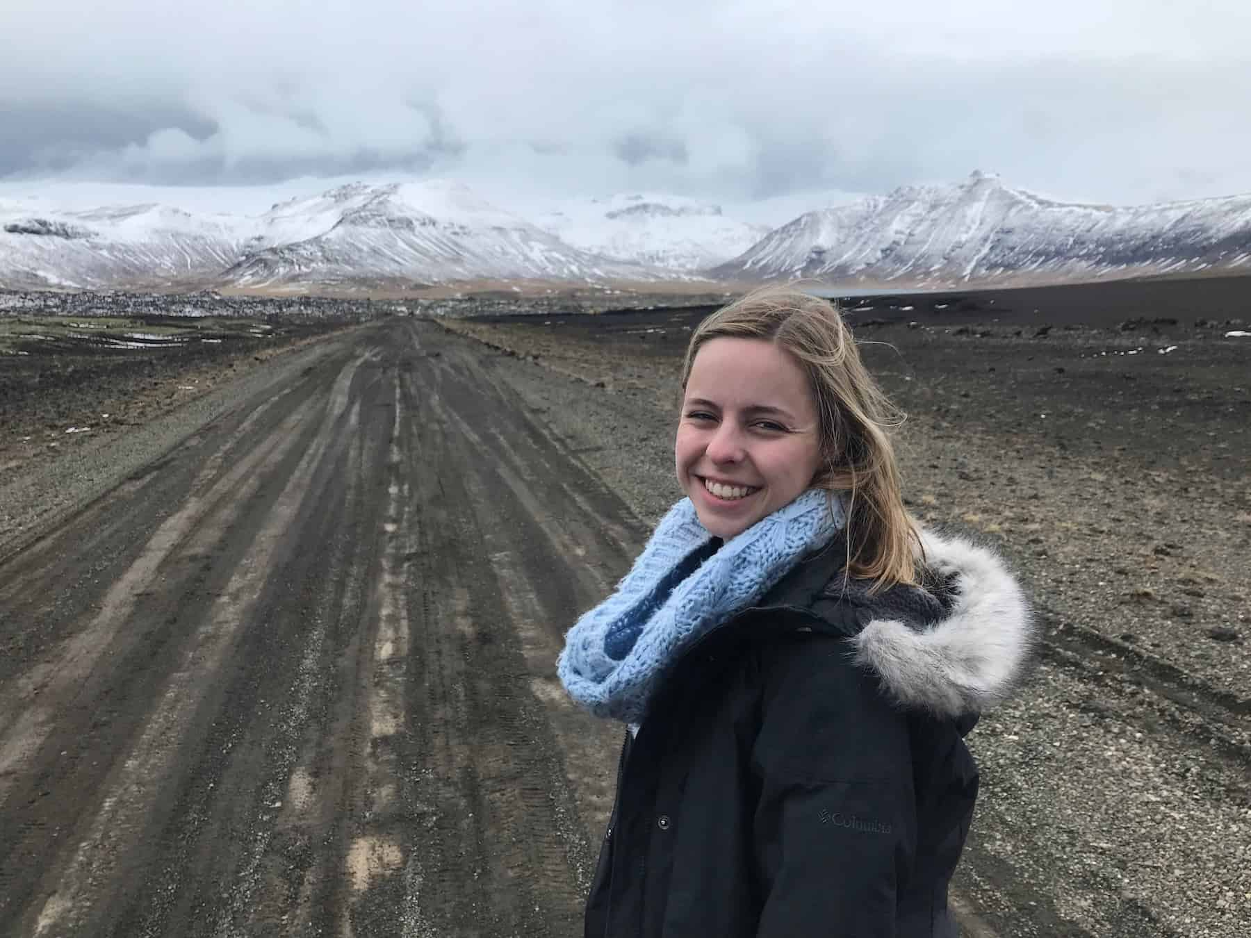 Woman smiling on a dirt road in the Snæfellsnes Peninsula in Iceland with snowy mountains in the background