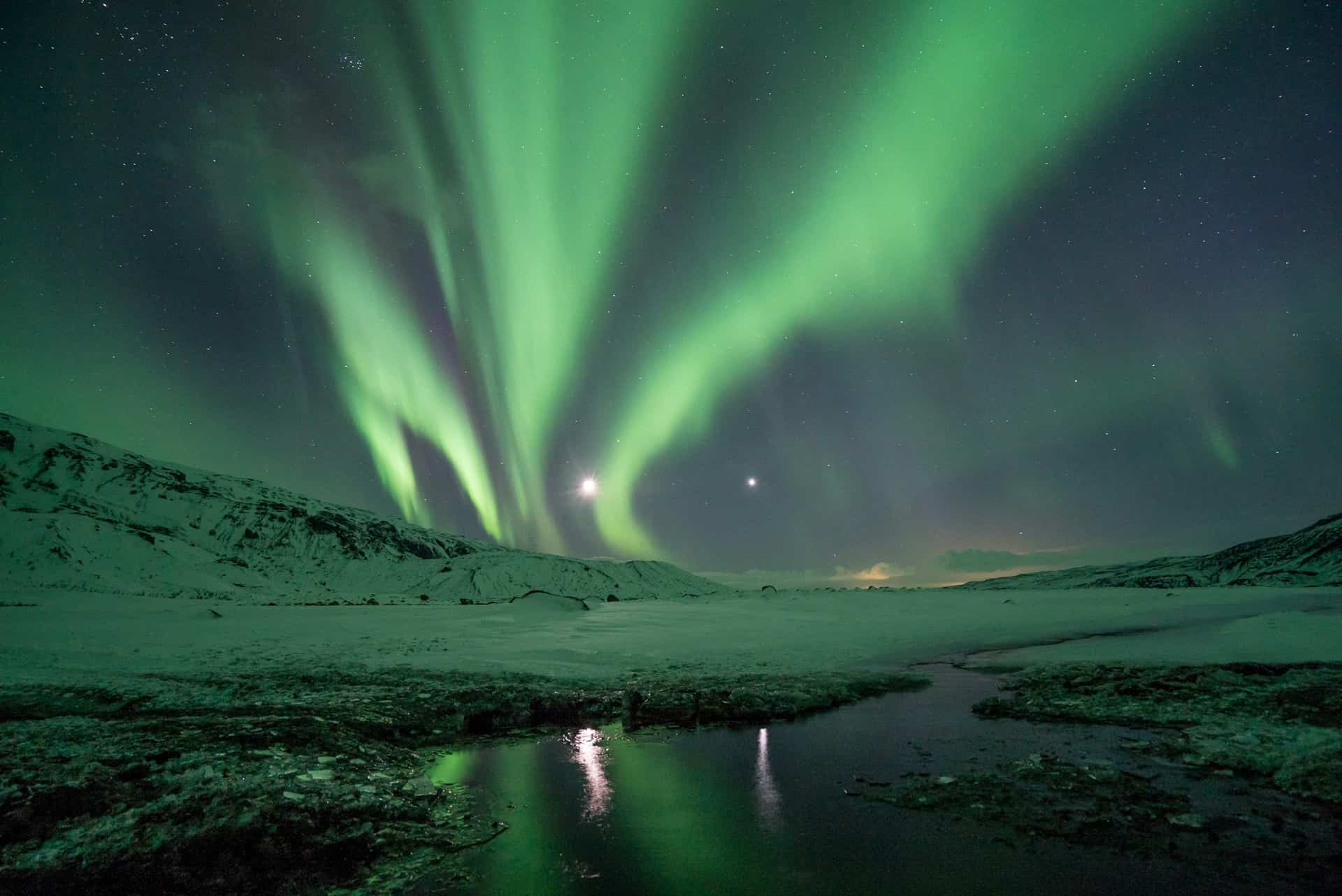 Green northern lights above a snowy mountain and lake in Iceland