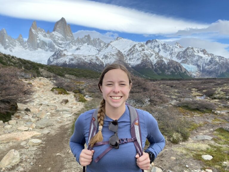 Woman smiling on a hiking trail with mountains in the background