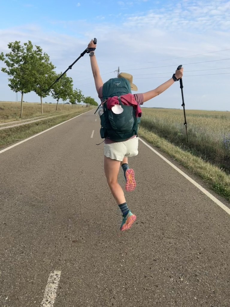 Hiker on an open road jumping up in the air with hiking poles and hands up