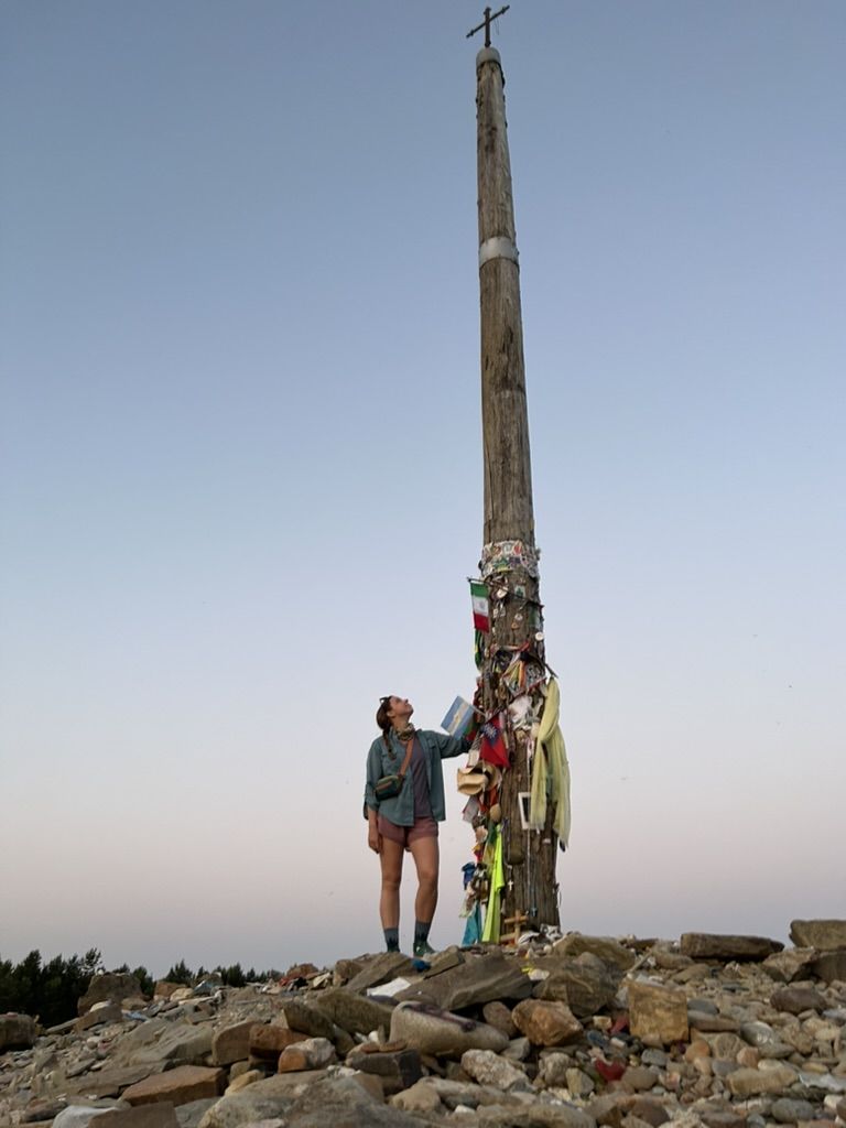 Hiker staring up at a tall cross at sunrise