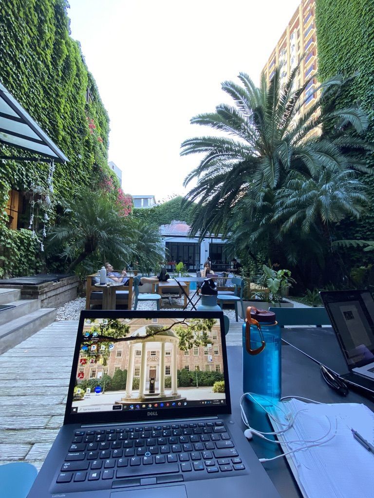 Laptop in a coworking space with palm trees and other green plants and people working in the background