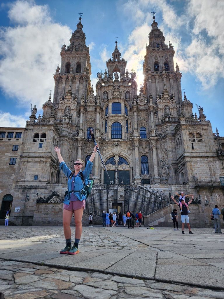 Woman standing in front of a cathedral with her hands and hiking poles up in the air