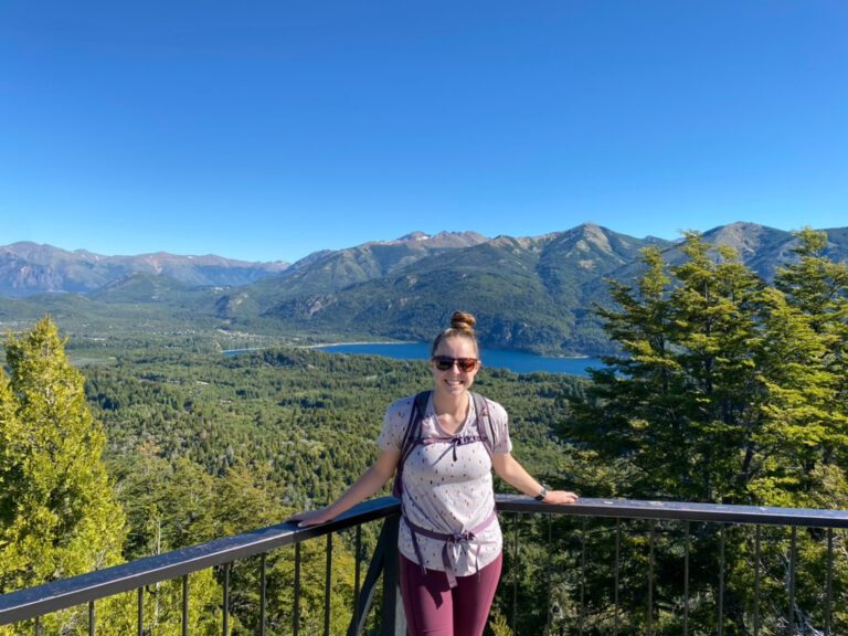 Woman smiling at an overlook of a bright blue lake surrounded by mountains in Bariloche, Argentina