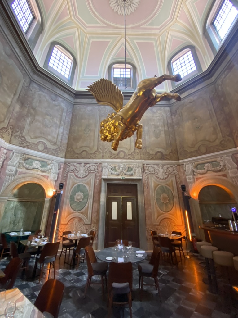 Dining area with elaborate painted walls and a golden flying lion hanging from the cieling at Palacio Chiado in Lisbon, Portugal