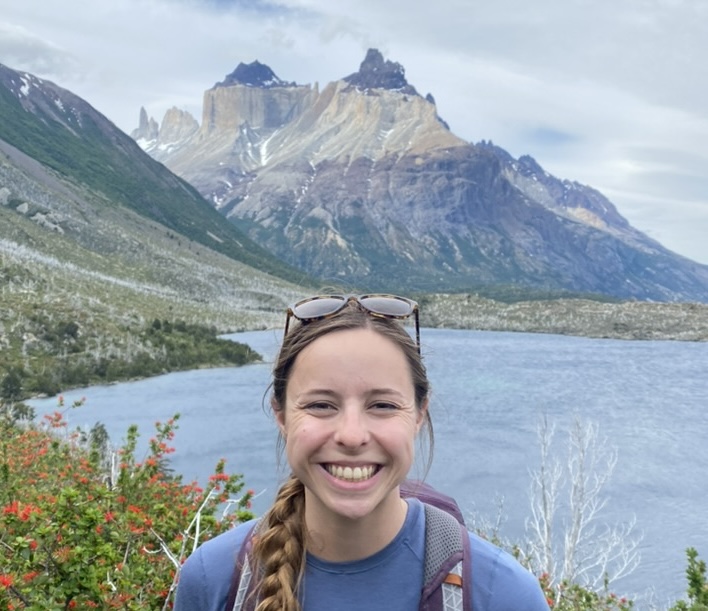 Blond haired woman with long braided hair smiling with a lake and mountain in the background