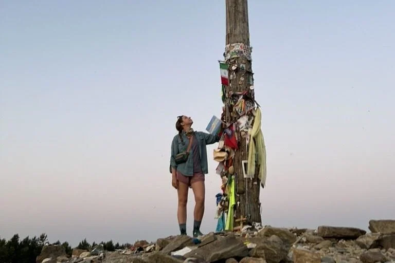 Hiker staring up at a tall cross at sunrise