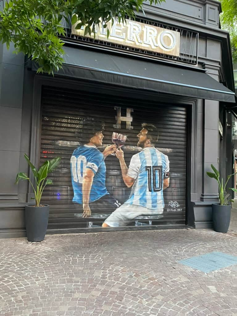 Painting of Diego Maradona and Lionel Messi clinking their glasses together.