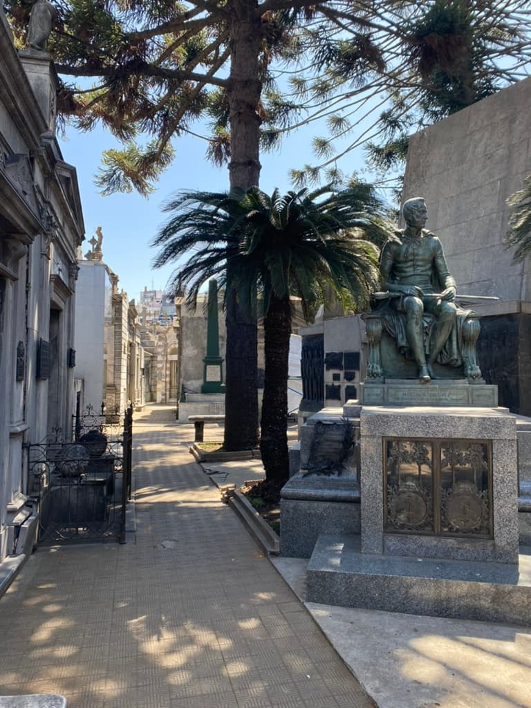 Recoleta Cemetery in Buenos Aires with mausoleums, a statue, and palm trees