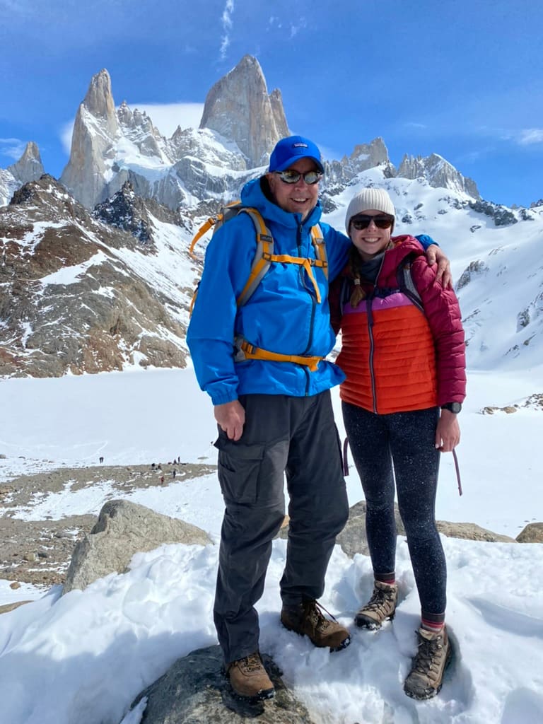 A father an daughter in coats at the top of Mount Fitz Roy in Argentina smiling in the snow