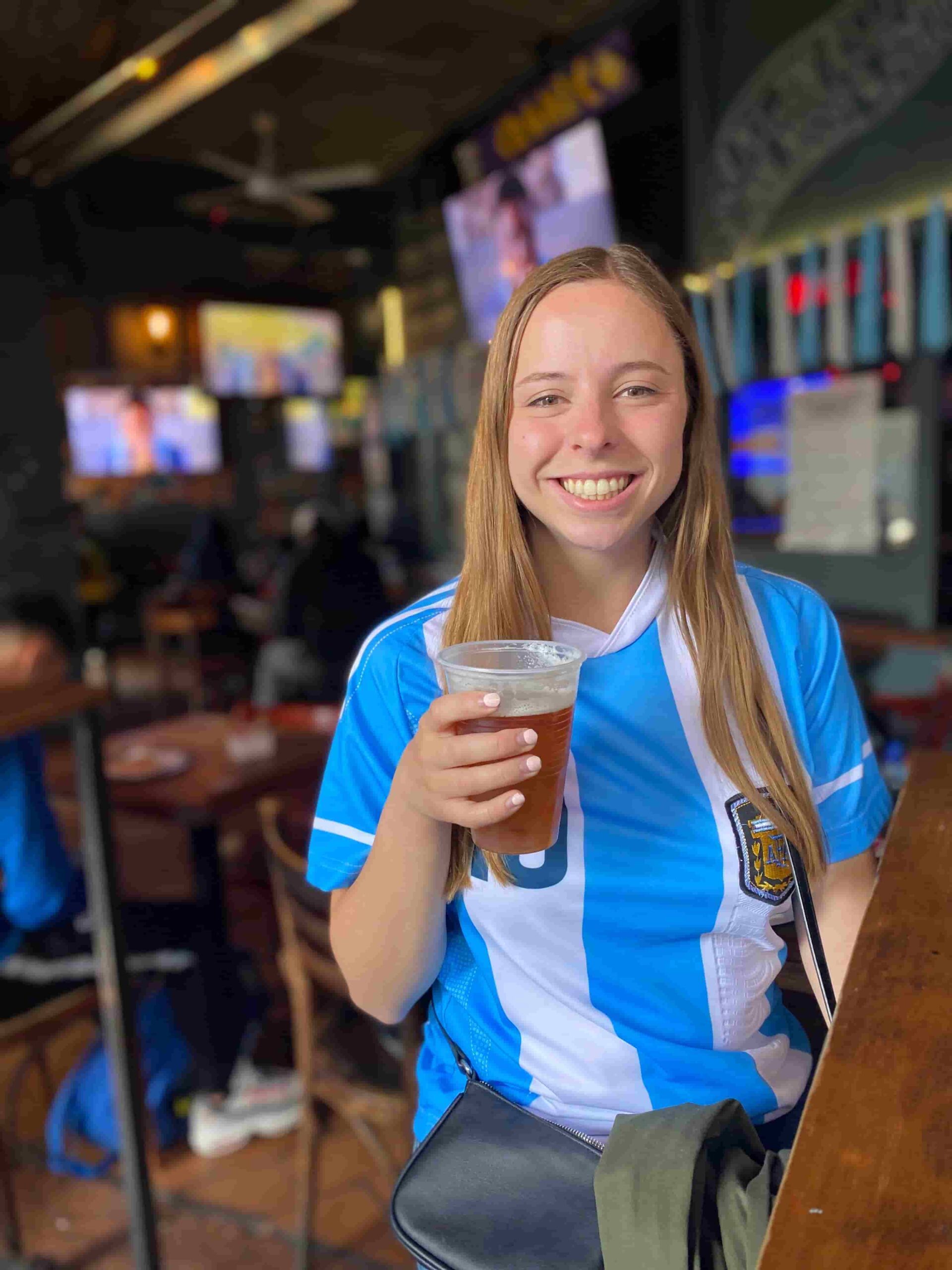 Woman smiling wearing a Messi Argentina jersey and holding a beer