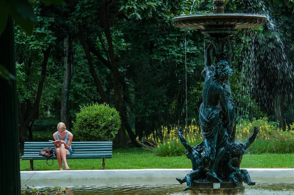 Young woman reading on a bench by a fountain in the Jardín Botánico in Buenos Aires