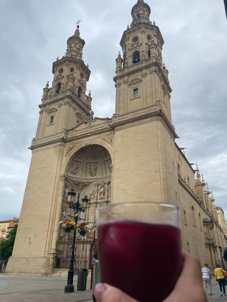 A hand holding up a tinto de verano in front of a cathedral in Logroño, Spain.