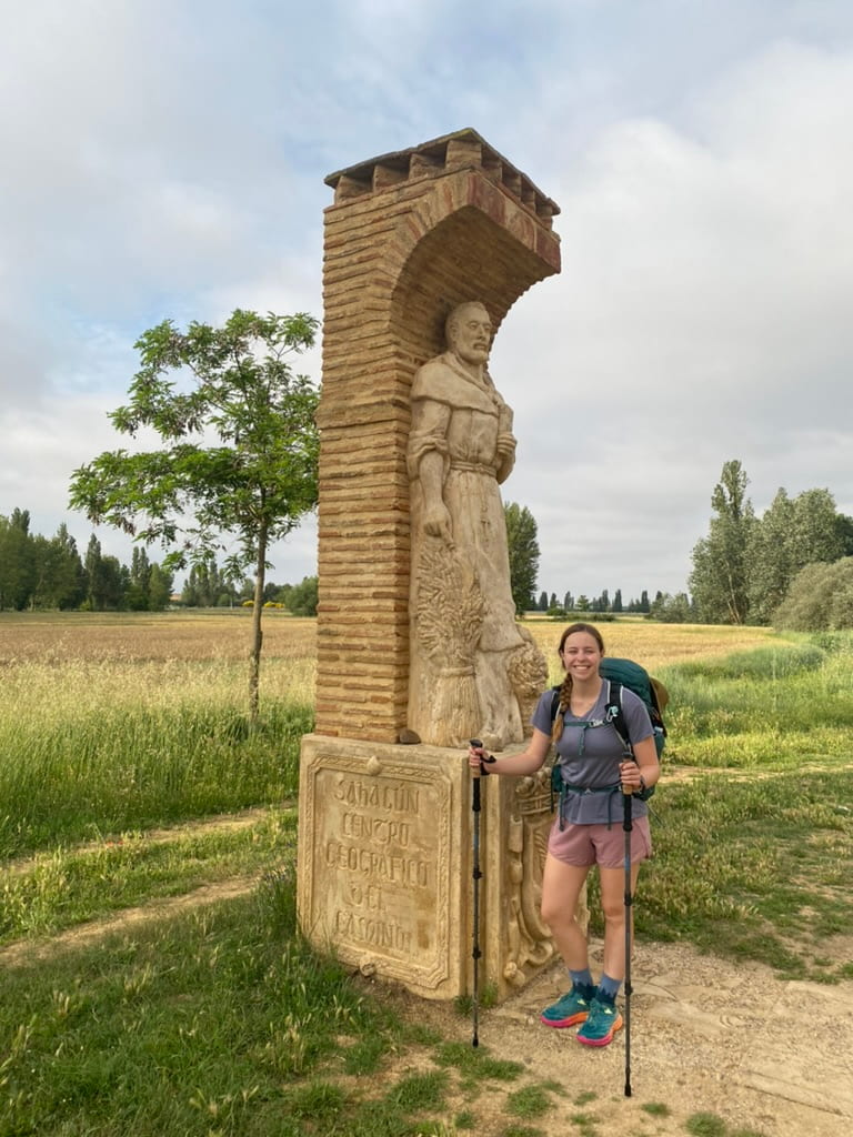 Female hiker smiling with trekking poles and a hiking pack at the halfway point of the Camino Francés route of the Camino de Santiago