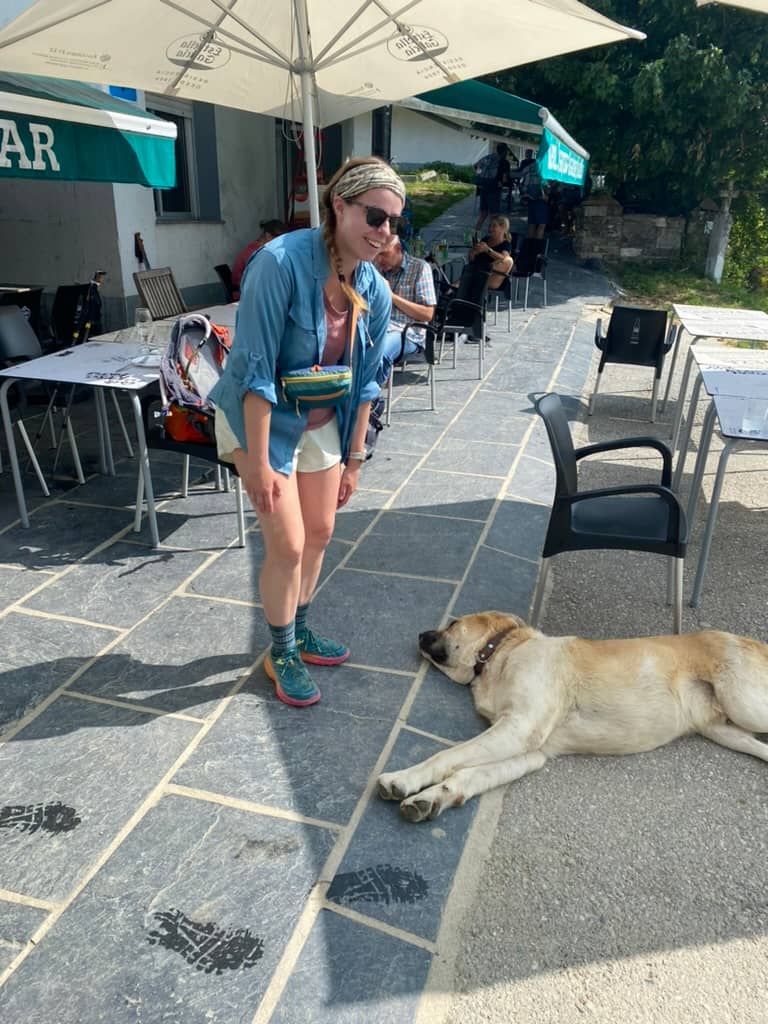 Woman wearing a fanny pack and smiling looking. down at a large dog on the Camino Francés.