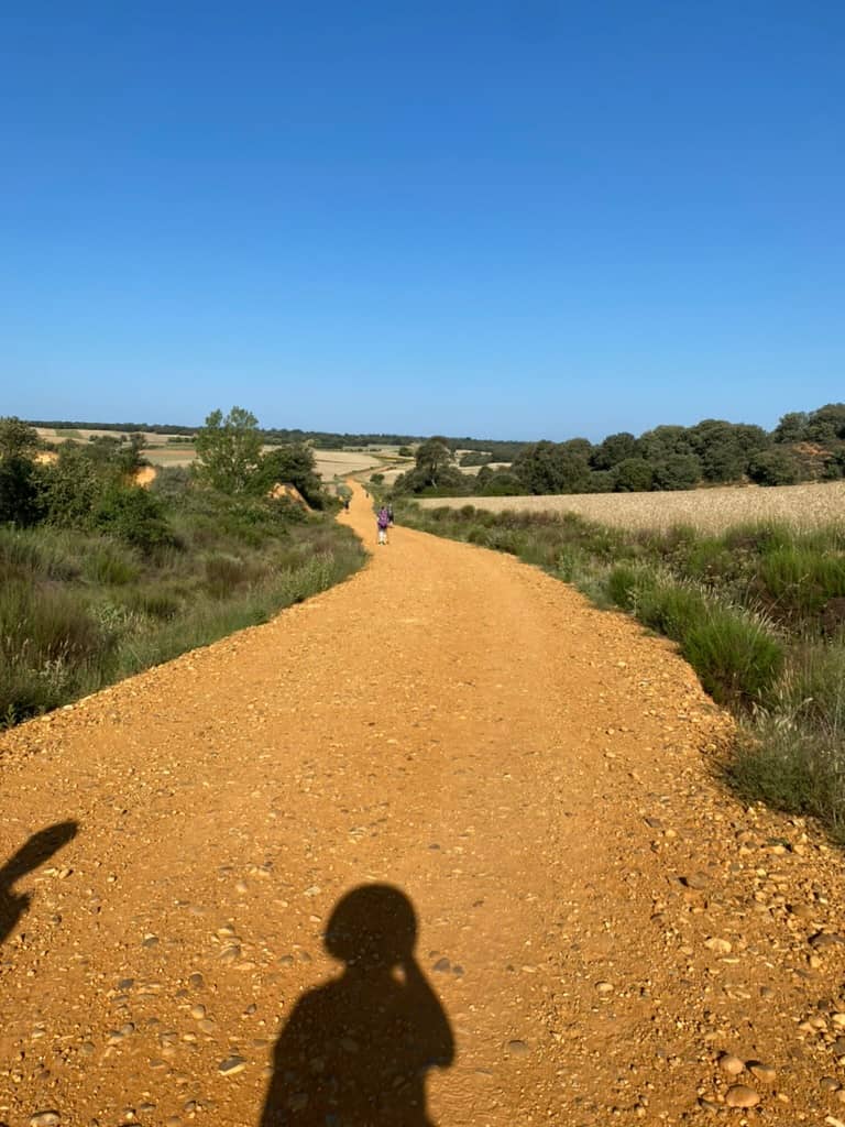 Dirt hiking path with a hiker's shadow on a hot day on the Camino de Santiago.