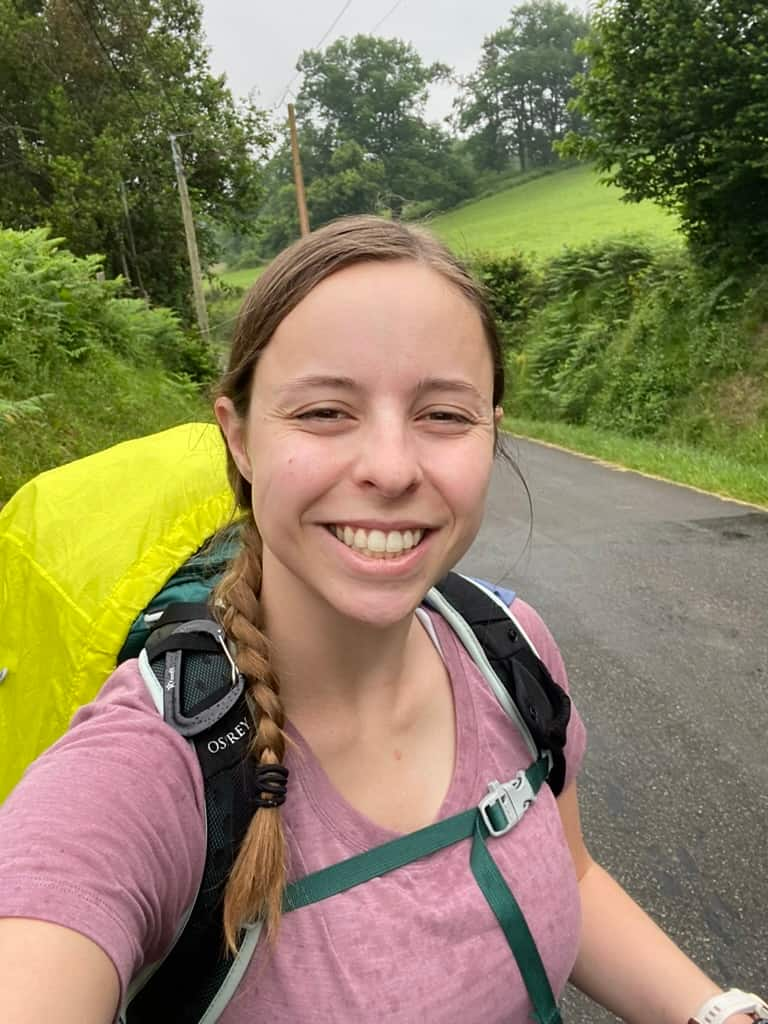 Female hiker smiling in t the rain while walking along a road with a hiking pack.