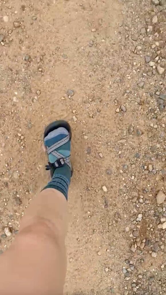 Foot stepping forward in socks and Chaco hiking sandals on a dirt road along the Camino de Santiago