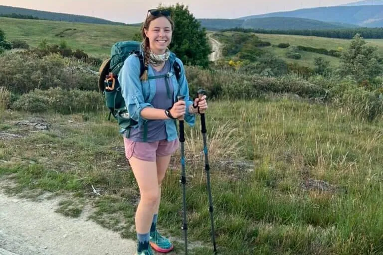 Hiker with a pack and trekking poles smiling in the early morning in the mountains