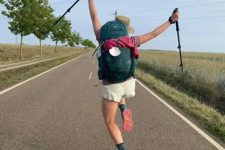 Mikala on an open road jumping up in the air with hiking poles and hands up.